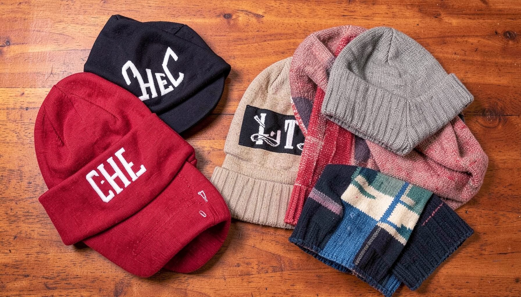 Flat lay of college-themed caps, beanies, and scarves arranged on a warm wooden tabletop